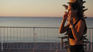 Portrait of attractive smiling happy brunette female runner running at seaside with airpods bluetooth headphones earphones. Healthy fitness athletic woman jogging outdoors. Motivation.