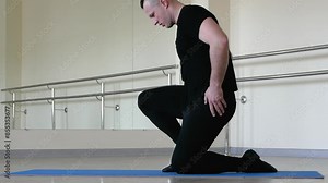 A professional dancer stretches during training performing body stretching exercises. A ballet dancer warms up in the fitness room, a man in jazz shoes and a classical uniform