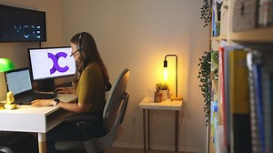 Premium stock video - Sliding reveal shot of a female working from home at desk on the computer and talking on the phone while typing