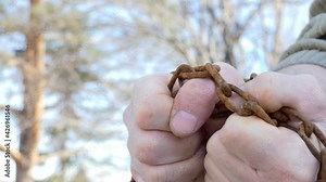 Chain, shackles. The man tries to break the rusty chain with his hands. Close-up shooting.