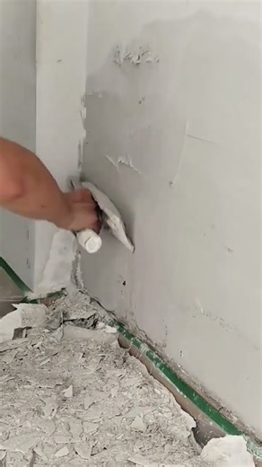 Worker scraping peeling plaster or paint from a wall with a flat scraper