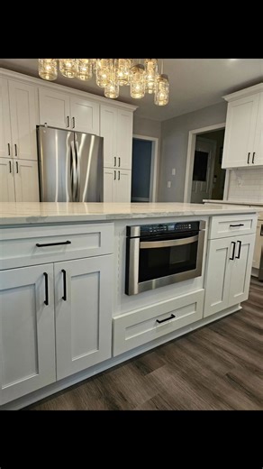 ✨ KITCHEN SPOTLIGHT✨ This kitchen renovation blends classic design with modern function, featuring white shaker cabinets and white quartz countertops with soft gray veining for a bright, timeless look. The subway tile backsplash adds subtle texture, with a framed herringbone accent above the stove that draws the eye and elevates the design. A pot filler adds convenience, while the farm sink brings both charm and practicality. Pantries flanking the refrigerator create smart storage, and a dedicat