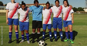 Female soccer team standing arm to arm on soccer field.