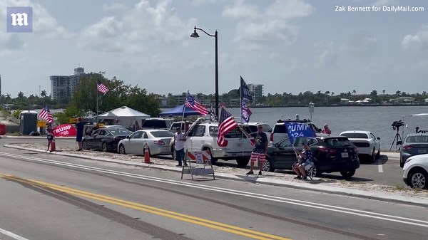 Trump supporters rally and wave flags behind Mar-a-Lago.