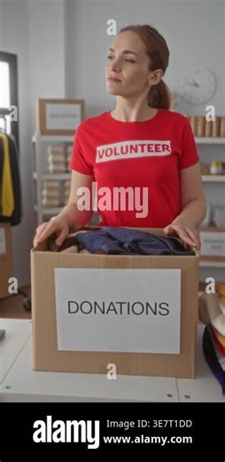 Young woman holds a cardboard donation box filled with clothes at a donation center building; charity compassion.