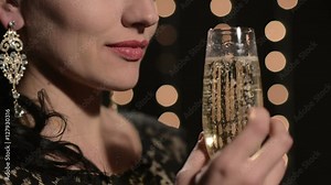 woman drinking champagne from a glass on a background of celebratory lights at night