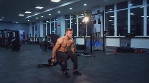 Handsome athlete training with dumbbells. Shirtless sportsman with muscular body lifting heavy dumbbells to the sides while sitting in the modern sports club.