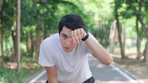 Slow motion of sportive young Asian man finishing running and bending over to catch breath.