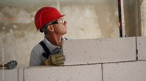 Bricklayer using rubber mallet hammer to tap and level concrete blocks wall. Contractor uses precise spirit bubble and laser level for brickwork. Worker constructs a wall in new apartment real estate.
