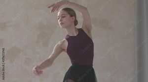 Beautiful young woman dancer in black stage dress rehearses dance moves. Dance lesson in studio with white parquet floors. Close up. Slow motion.