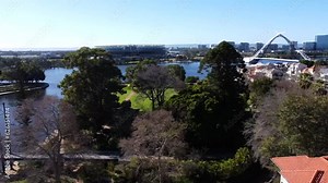 Drone Aerial View travelling sideways over East Perth foreshore park with Matagarup Bridge to Suspension pedestrian bridge with Optus Stadium and Swan River