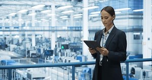 Thoughtful Female Engineer Monitoring and Analyzing Conditions at a Modern Tech Electronics Factory with Automated Robot Arms Working with the Help of Artificial Intelligence Software