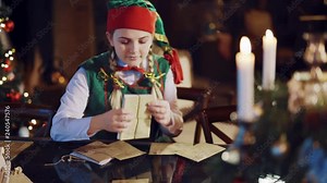 A jolly elf looks through a stack of envelopes with wishes and happily dances against the background of candles and a fireplace in the room. Mail for Santa Claus