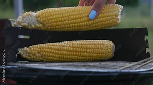 Young woman with beautiful manicure collect ears of corn on the grill