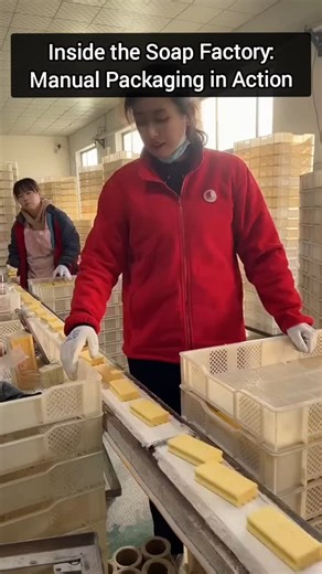 AI Overviews | Artificial Intelligence and Technology News on Instagram: "A manual packaging process is underway in a soap factory, where workers handle freshly molded soap bars with care. As the bars move steadily along a conveyor belt, employees transfer each one into plastic crates strategically placed around the workspace. The environment is clean, orderly, and well-organized, with neatly stacked crates in the background—highlighting a systematic and efficient approach to packaging. This han