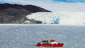 Greenland. Little red sailboat cruising among floating icebergs in Disko Bay glacier during midnight sun season of polar summer. Studying of a phenomenon of global warming. Unesco world