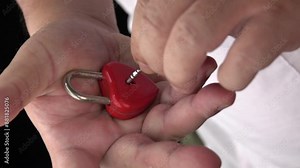 A person is holding a red heart shaped lock with a keyhole. The person is holding the lock in their hand, and it is a special or sentimental item