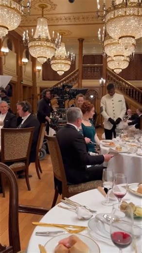 Titanic BTS: First-Class Grand Dinner Scene With Rose at the Table 💎🍽️ Step behind the camera and see how the elegant first-class dinner scene was filmed. The grand dining hall is recreated with spectacular chandeliers, golden pillars, and the iconic staircase glowing in the background. Extras in formal attire surround the table while Rose sits gracefully, maintaining her aristocratic posture. The cinema camera rolls in front of her, capturing fine emotional detail. Meanwhile, the iPhone POV r