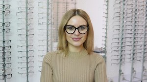 Attractive young blonde woman wears transparent glasses with black frame for vision correction in an eyewear store. Vision correction concept