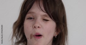 Cheerful schoolgirl with birthmark playfully winks eyes on white background. Joyful girl makes funny faces entertaining friends during school break