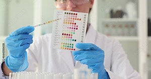 Hand holds pH indicator and compares color with scale. Testing acidity of liquids