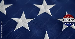 Vote button pin, in the red white and blue of the United States America, pinned to the American flag. Encouraging voting, national pride, and political involvement in the US elections.