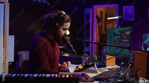 Sound engineer recording backing vocals and singing on microphone, using daw software and mixing console in home studio. Artist listening to mixed tracks and create a good acoustic audio. Camera B.