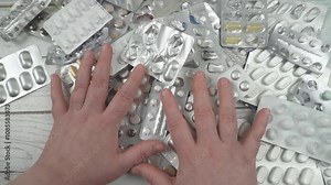 Pill packs of different sizes and shapes are randomly stacked together. Women's hands are sorting through blisters in an attempt to find the right pills