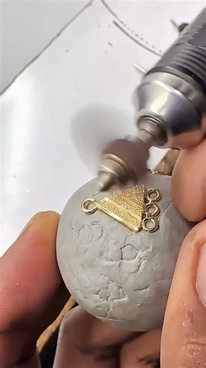 Rotary tool polishes gold-toned triangle held steady in clay, refining loops with delicate