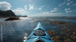 Kayaking on a sunny day, view from the kayak. Ocean waves, blue water, and seaweed are visible. Rocky coast in the background.