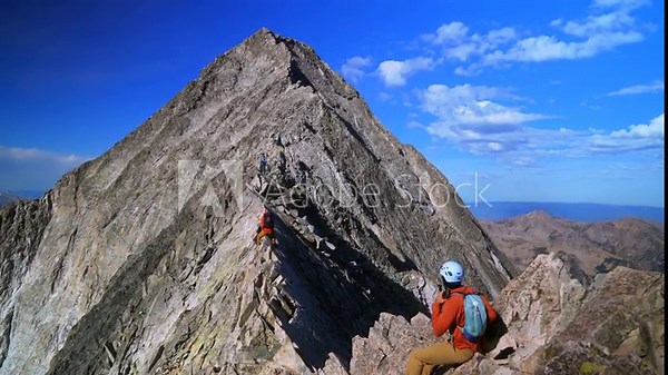 Knifes Edge Capitol Peak north east ridge Wilderness Trail Hikers scrambling rock climbing across Rocky Mountains Colorado 14er mountainside large boudlers aerial view summer blue sky sunny morning