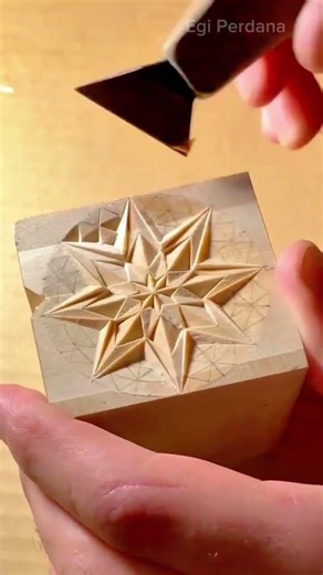 carving a geometric star pattern into a wooden block using a specialized chip carving hand tool
