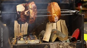 Large chunks of delicious pork hams cooked on an open fire. The street food. Food outdoors. Camping and cooking on a spit over the fire, man cooks large pieces of meat on a spit on fire, closeup