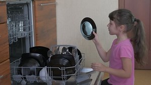 Child with washing machine. A happy child open a dishwash machine and takes off the plate from it in the kitchen.