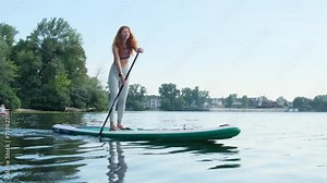Woman gracefully navigates paddleboard across serene lake. Woman shows adept maneuvering skills with each precise stroke of paddle