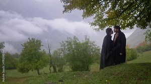 Happy young LGBT couple kissing in the rain under a tree in a fairytale valley among the mountains