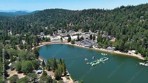 tilt aerial footage of the green waters of Lake Gregory with a jungle gym on the water, boats, homes along the hillside, cars and lush green trees in Crestline California USA