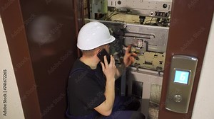Emergency situation in elevator equipment. An engineer, worker, electrician near an open elevator shaft talks on the phone with technical support. Verifies performance indicators before repairs.