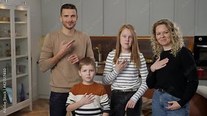 Positive parents and redhead kids with hearing loss using sign language to send peaceful message while posing at home. Portrait of smiling mute family gesturing and showing heart shape with fingers