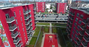 New red buildings with painted roses in a secure residential complex with parking lots and a playground during the summer in Poland. Dynamic 4K drone footage captures the scene.