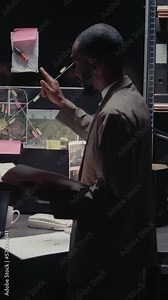 Vertical video: Two inspectors checking background records in evidence room, looking at surveillance footage for private investigation. Team of police officers uncovering details on map and case files