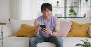 Gen Z queer man non-binary sitting easy relax happy read news on web page app at home sofa. Asia people LGBT young adult guy play web3, store shop e-commerce buyer, virtual retail network cyber paying