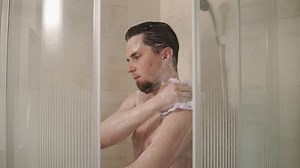 Man is washing himself in the morning in a shower cabin indoor. He is sponging his body using shower gel. Man using shower after gym. Hygiene.