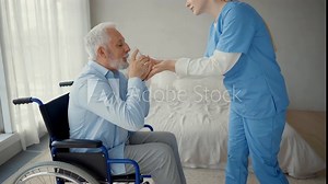 Nurse helps old wheelchair man standing. Physical therapist woman provides medical help support to senior paralyzed male giving hands. Palliative care in late stage of neurodegenerative pathologies.