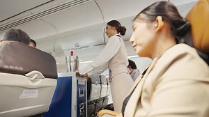 4K Asian woman flight attendant serving food and drink to passenger on airplane.