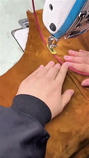 stitching a brown fabric using a sewing machine to create a garment for a fashion design project