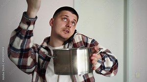 A man calls a roof repair service while collecting leaking water from the ceiling in a pan.