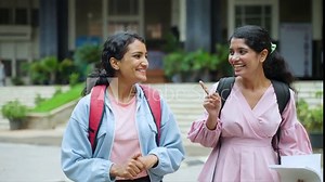tracking shot of Happy smiling college girl students going home by talking each other after classes at college campus - concept of taking break, friendship and bonding.