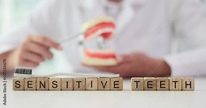 Phrase Sensitive Teeth composed of small wooden cubes with toothbrush on top against dentist. Specialist gives lecture using jaws model