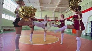 Slow motion shaky camera video, group of beautiful long legged girls jumping in circle facing inwards with pom-poms at cheerleading practice in school gymnasium, low angle Stock Video